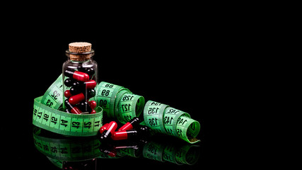 Glass bottle with diet pills and measuring tape  on black background