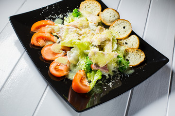 Caesar salad with bacon and quail eggs Black plate on a white wooden