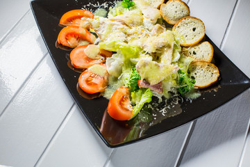 Caesar salad with bacon and quail eggs Black plate on a white wooden