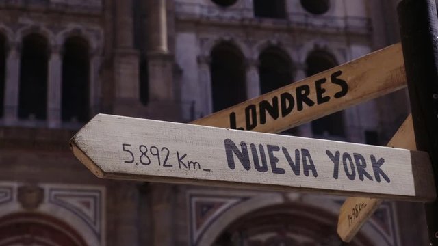 A wooden post with a road sign that points to London, Paris and New York 