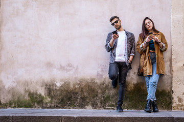 Fototapeta na wymiar Two young people using smartphone outdoors against a white wall