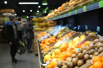 Background of supermaket with different fruits. Blurred image of customers choosing fruits.