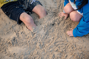 Child pours sand on his feet on sand beach in summer.
