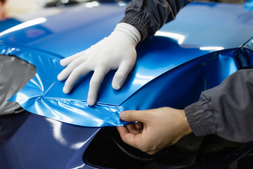 Car wrapping specialist putting vinyl foil or film on car. Selective focus.