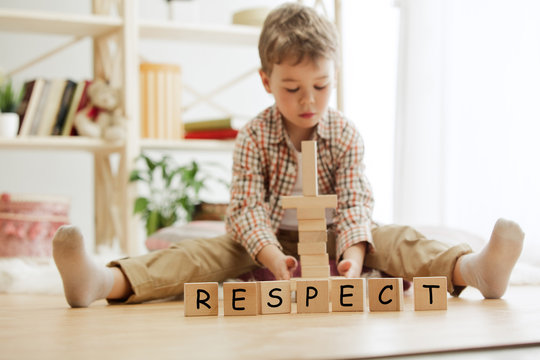 Wooden cubes with word RESPECT in hands of little boy at home. Conceptual image about child rights, education, childhood and social problems.