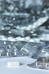 One single tablet in front of many empty blister packages on white background, drug misuse concept