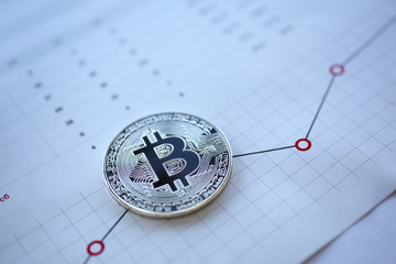 Silver bitcoin sign coin lying at stats graph paper closeup