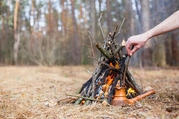 Naklejka premium At the stake in the spring forest, a clay Turkish coffee pot is heated against the grass. In the frame one man's hand.