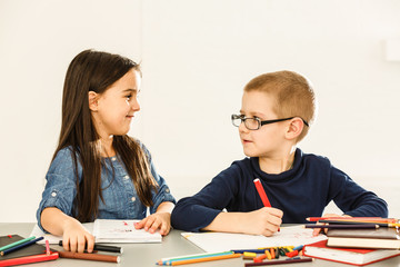 Two smiling little kids at the table draw with crayons, isolated on white