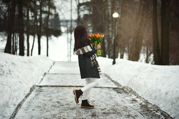 Young girl with orange tulips walking in a park