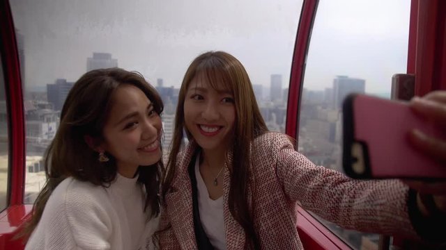 Two beautiful friends talking pictures together riding large ferris wheel. HD, Slow motion