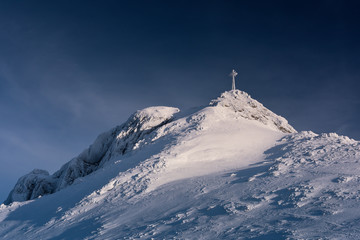 Snow covered cross on the mountain top Giewont.