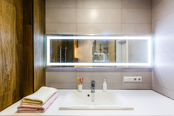Fototapeta na wymiar White and brown bathroom boasts a nook filled with double vanity cabinet topped with white and grey counter paired with tile backsplash under framed mirror
