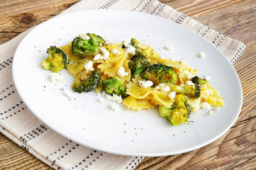 plate of boiled butterfly pasta with fried in garlic oil broccoli, feta, and black pepper on napkin. warm wooden background