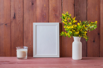Mockup with a white frame and branches with yellow flowers in a vase on a wooden table
