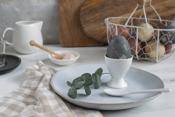 Easter breakfast table setting idea, minimal decoration - eucalyptus branch, porcelain egg cup, dyed egg, blue plate, spoon