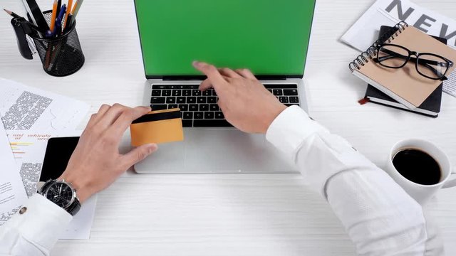 partial view of businessman using laptop and holding credit card at workplace