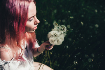beautiful girl with pink hair sits in a high field with dandelions in the summer 