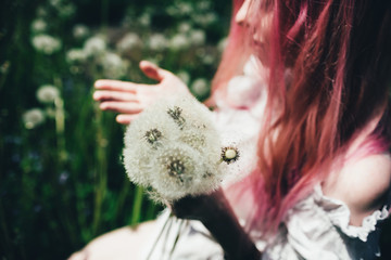 beautiful girl with pink hair sits in a high field with dandelions in the summer 