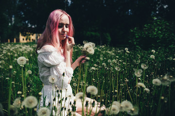 beautiful girl with pink hair sits in a high field with dandelions in the summer 