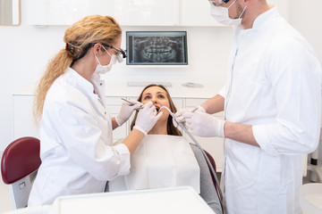 Obraz premium Zahnärztin behandelt Patientin, Assistent hält Sauger