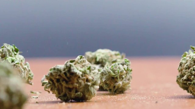 Slow motion cannabis buds falling over a wooden table. 120fps.