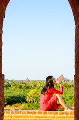 girl sitting on rim of Myanmar pagoda ruin, looks aside, at Bagan, Myanmar