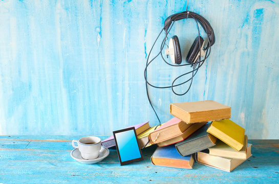 audio book concept, with stack of books, headphones, smartphone and cup of coffee, panorama, good copy space