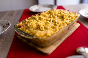 Baked pasta with cheese in a glass dish on a wooden table with a red cloth.