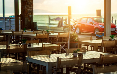 Beach cafe by sea at sunset on waterfront with parked cars beach. Depth of field, focus blur, beige toning, Crete, Greece