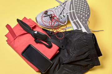 running shoes with a pair of shorts, a red towel and technological accessories on a yellow background