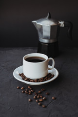 White cup of coffee and coffee maker on dark background