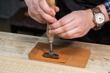 Man makes a stamp on the leather textile at a workshop. Concept of handmade craft production of leather goods.