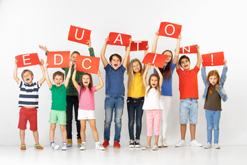 Education gives the way of life. Group of happy screaming children or young team with a red banners isolated in white studio background. Education and advertising concept, human rights.
