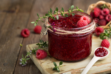 Raspberry jam in a glass jar and fresh raspberry and thyme