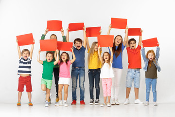 Group of happy screaming children with a red empty banners isolated in white studio background. Education and advertising concept
