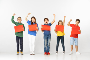 Group of screaming serious children with red empty banners isolated on white studio background. Education and advertising concept. Protest and children's rights concepts.