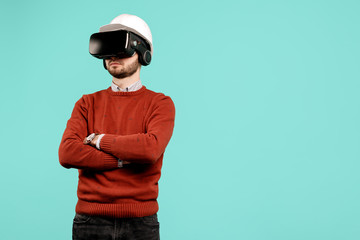 Attractive young handsome bearded engineer or constructor man in casual outfit wearing vr goggles over cyan background. Architecture and Renovation concept.
