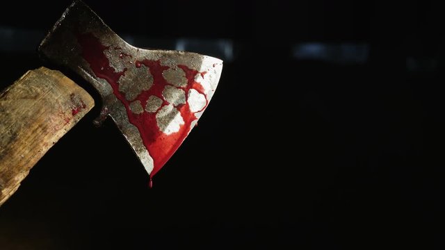 Axe with blood in hand on the dark background
