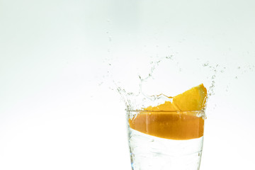 Slice the orange slice in a glass of water and make a spray on a white background. water spray in the air. a slice of citrus drops in a glass spray.