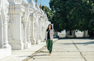 single Asian girl leans on white pagoda at Kuthodaw Pagoda, Mandalay, Myanmar