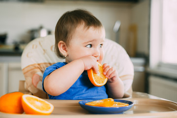 little girl sitting in baby chair, eating an orange