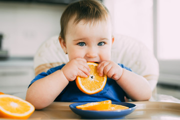 little girl sitting in baby chair, eating an orange