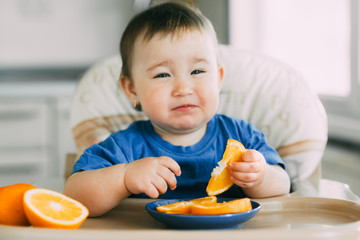 little girl sitting in baby chair, eating an orange