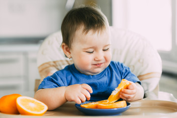 little girl sitting in baby chair, eating an orange