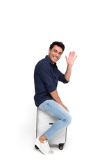 Smiling tourist sitting on travel bag and saying hello isolated over white background © comzeal