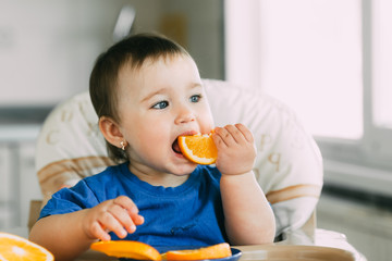 little girl sitting in baby chair, eating an orange