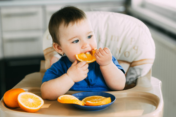 little girl sitting in baby chair, eating an orange