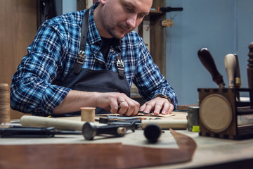 Man making leather wallet at a workshop. Concept of handmade craft production of leather goods.