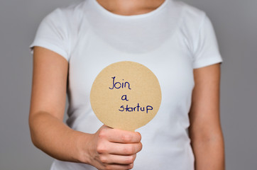 Young women  showing   round cardboard paper     with handwritten blue  text  - Join a Startup.